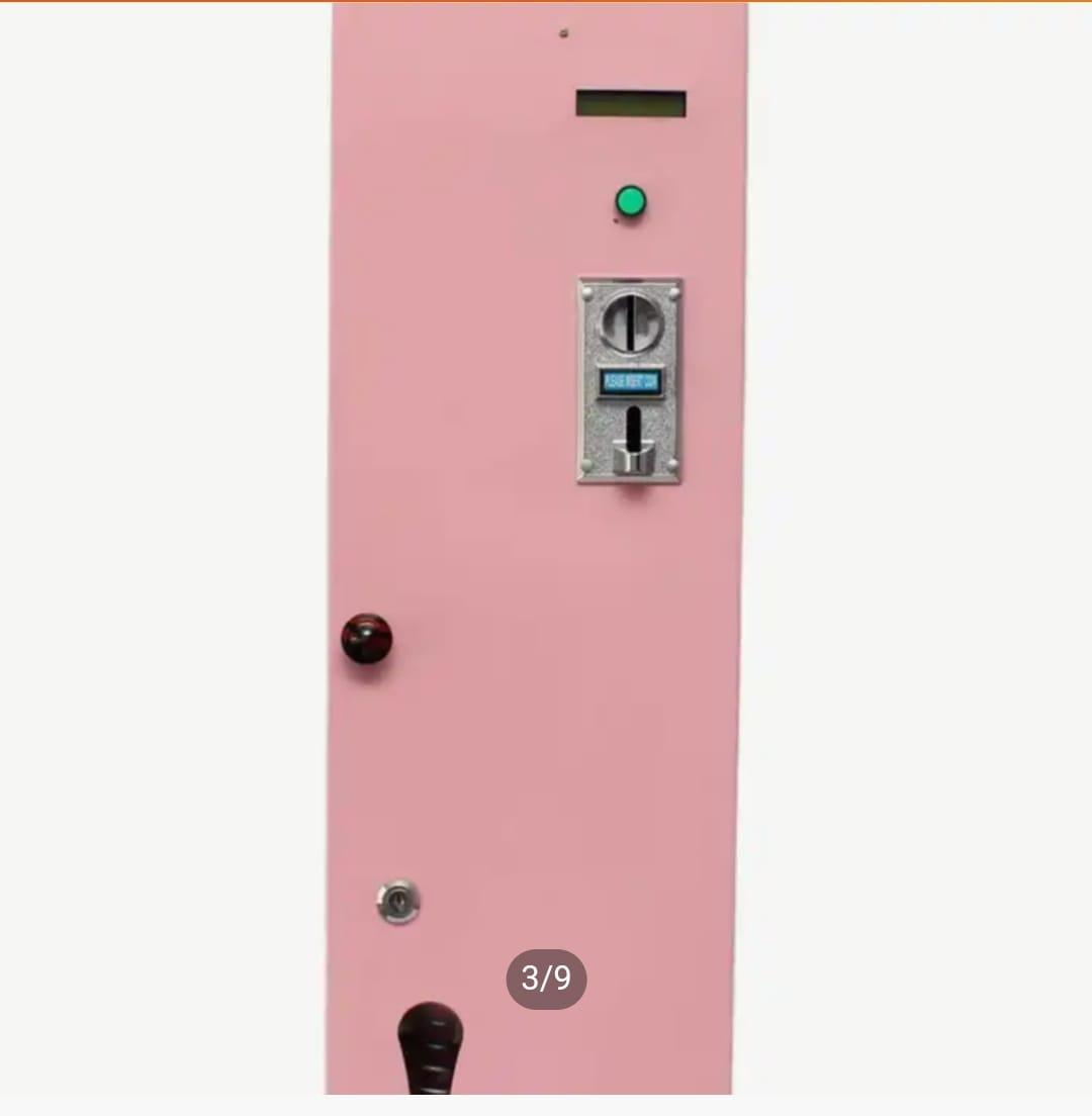Front panel view of a pink wall-mounted contraceptive vending machine featuring coin slot, status light, and key lock.