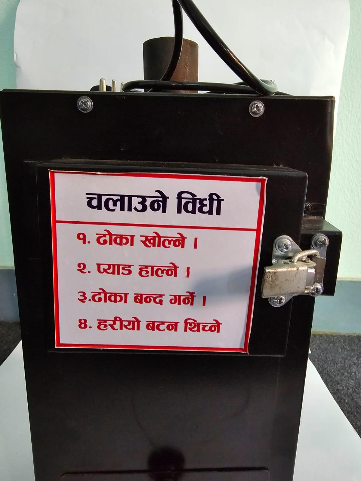 Detail view of the disposal chamber door on a black sanitary napkin incinerator highlighting step-by-step Nepali usage guidelines.