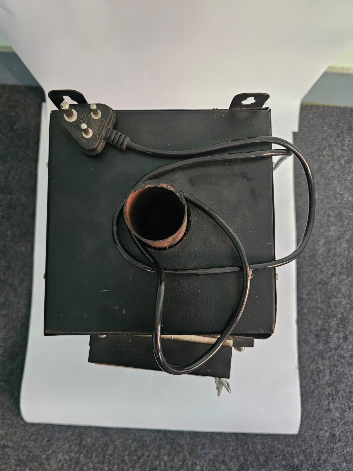 Top-down view of a black electric sanitary pad disposal unit showing the central exhaust chimney pipe and 3-pin power cord.