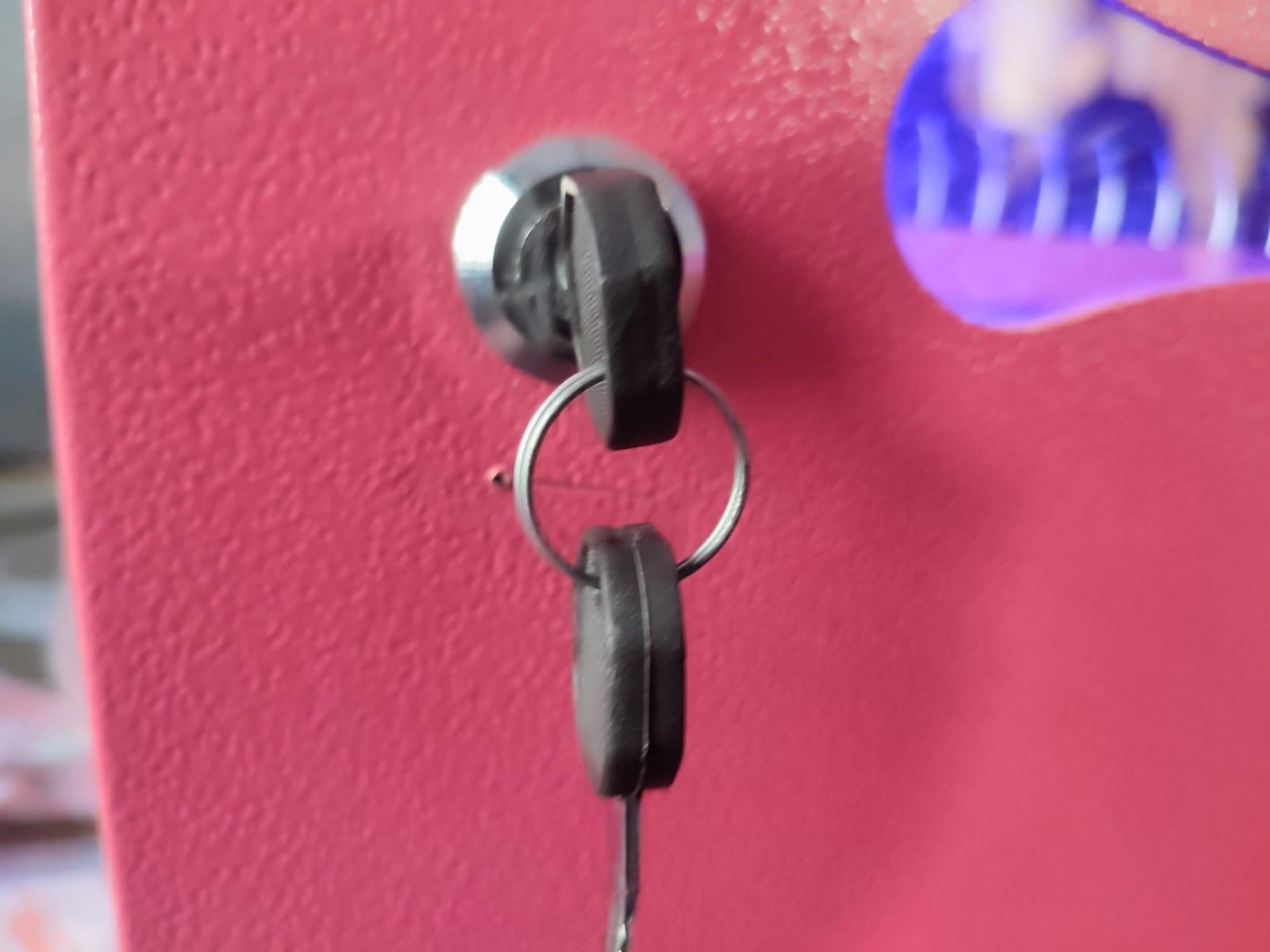 Close-up view of a metal cylinder lock and keys inserted into the pink metal front door of a vending machine cabinet.