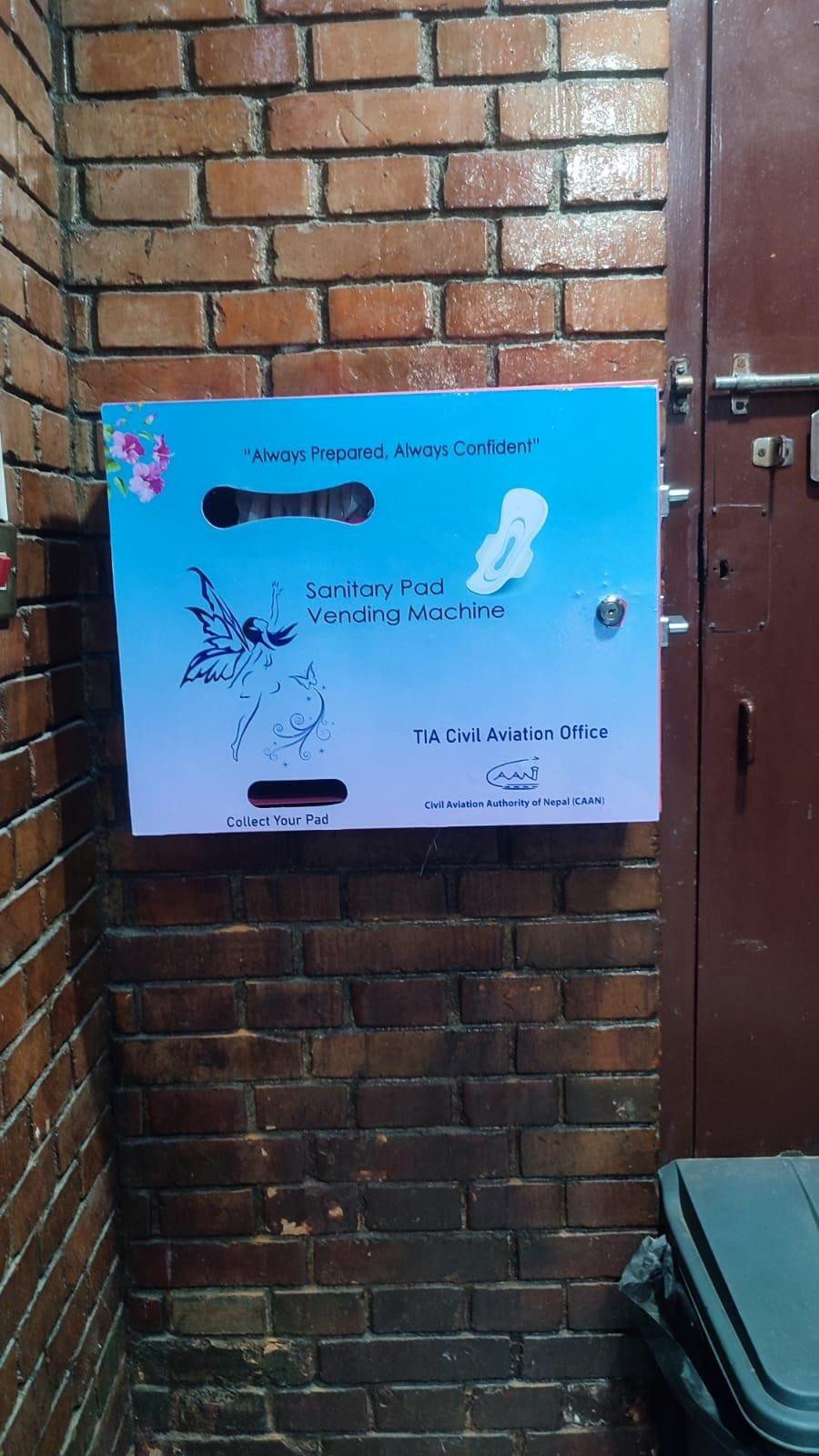 Wall-mounted sanitary pad vending machine branded for TIA Civil Aviation Office installed against a brick wall.