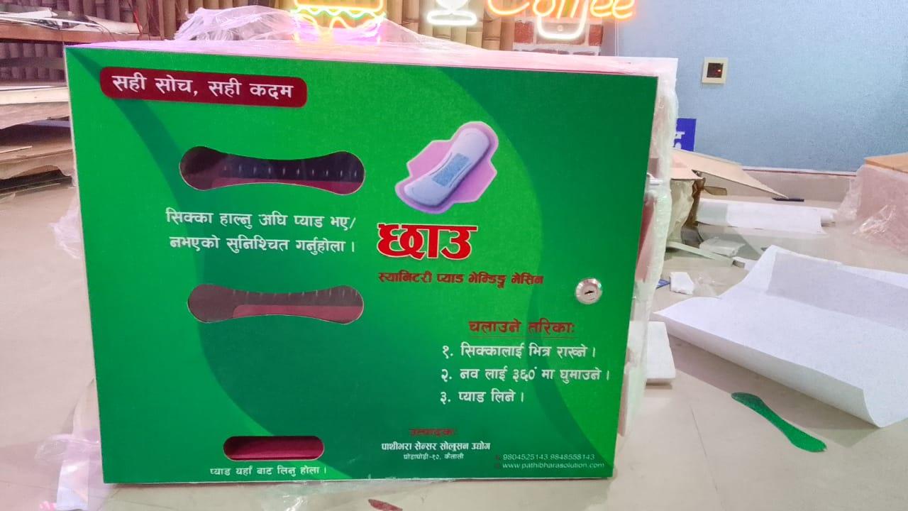 Green manual sanitary pad vending machine box featuring Nepali instructional text and dispensing slot.