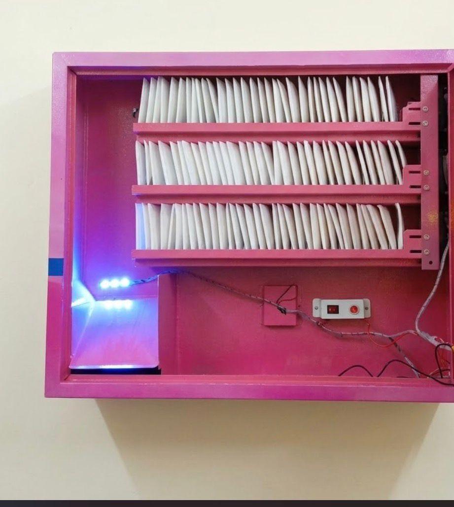 Open interior view of a pink sanitary pad vending machine showing multi-tier spiral storage racks and LED chute lighting.